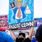 a protestor holding a placade depticting donald trump as a fascist clown