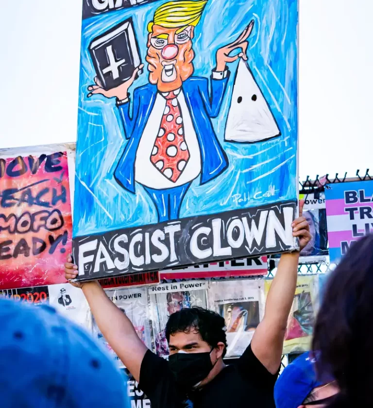 a protestor holding a placade depticting donald trump as a fascist clown