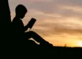 A silhoutte of a boy reading a book at sunset - educational disparity