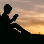 A silhoutte of a boy reading a book at sunset - educational disparity