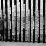 A man looking through a border fence.