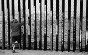 A man looking through a border fence.