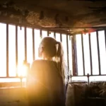 A woman looking through bars with the sunrise in front