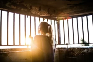 A woman looking through bars with the sunrise in front