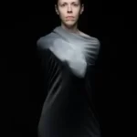 A person set against a black background bounded in a garment