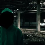 a faceless and hooded social actor in an abandoned building