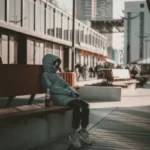 A working class boy sat on a bench wearing a hoody