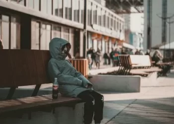 A working class boy sat on a bench wearing a hoody