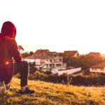 a man sat looking over a field at sunset