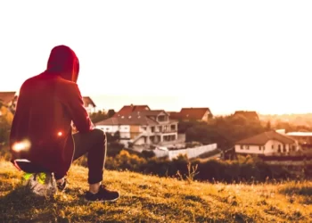 a man sat looking over a field at sunset