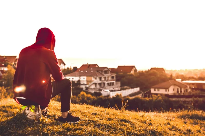 a man sat looking over a field at sunset