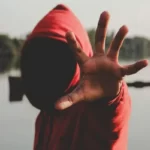 A hooded working class person with their hand splayed towards the camera