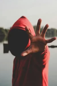 A hooded working class person with their hand splayed towards the camera