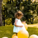 A young girl playing with balloons against a park background.