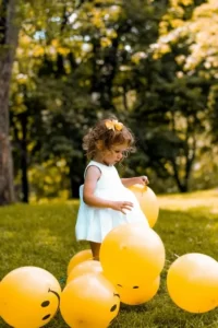 A young girl playing with balloons against a park background.