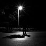 A shadowy deviant dangerous classes figure under a streetlight