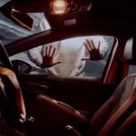 A shot taken from inside a car looking outwards through the passenger window. A person ominously has their hands pressed against the window