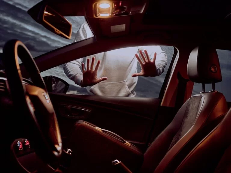 A shot taken from inside a car looking outwards through the passenger window. A person ominously has their hands pressed against the window