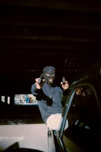 A man wearing a balaclava at night and pointing two guns akimbo at the camera