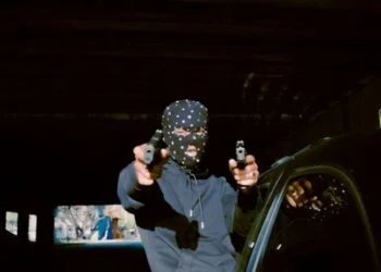 A man wearing a balaclava at night and pointing two guns akimbo at the camera