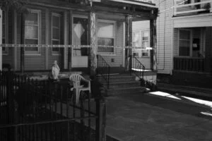 a black and white crime scene showing the front facade of a house cordoned off with police tape - neoliberalism