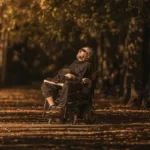 A disabled man in a wheelcahir looking throughtful against a backdrop of an autumnal forest