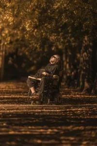 A disabled man in a wheelcahir looking throughtful against a backdrop of an autumnal forest