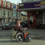 a sombre disabled man in a wheelchair with a shopping trolley