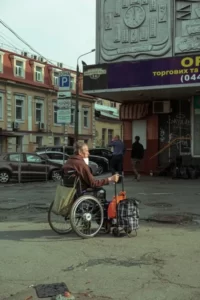 a sombre disabled man in a wheelchair with a shopping trolley