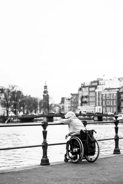 a disabled person alone by the river wearing a hoody and sitting in a wheelchair