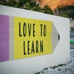 A white wall with a mural in the shape of a pencil and reads 'love to learn'