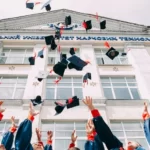 The arms of university students celebrating by throwing mortarboards into the air in front of a building
