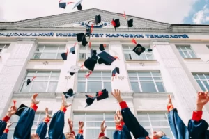 The arms of university students celebrating by throwing mortarboards into the air in front of a building