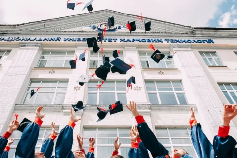 The arms of university students celebrating by throwing mortarboards into the air in front of a building