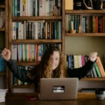 a teenage girl sat at a laptop, celebrating a-level attainment
