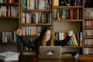 a teenage girl sat at a laptop, celebrating a-level attainment