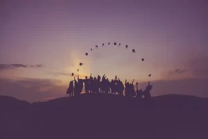 A line of graduates at sunset throwing their mortar boards in tair