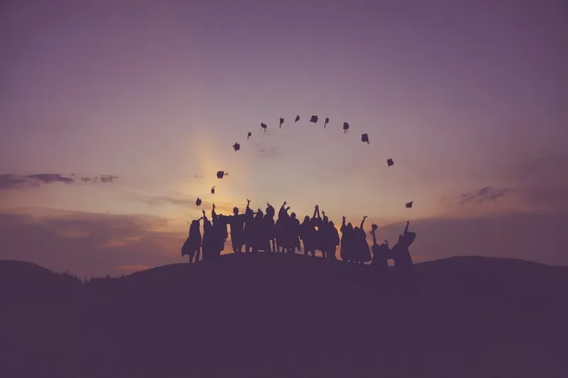 A line of graduates at sunset throwing their mortar boards in tair