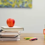 a stack of education books and an apple on a table