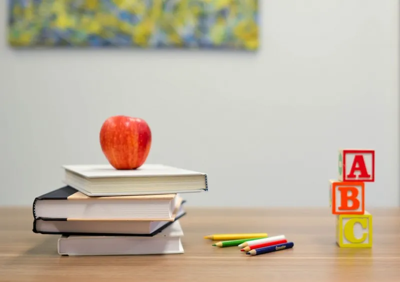 a stack of education books and an apple on a table