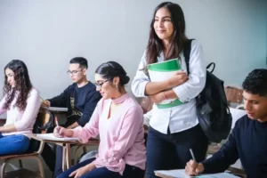 A student in a education classroom standing up. Other students are sat down.