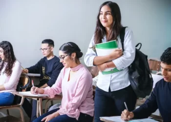 A student in a education classroom standing up. Other students are sat down.