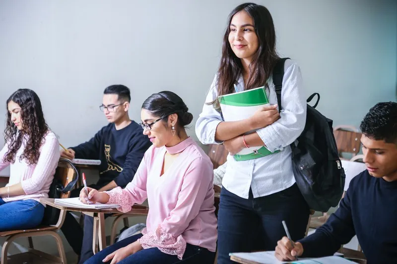 A student in a education classroom standing up. Other students are sat down.
