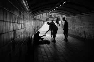 black and white image of people donating money to a homeless person sat on the floor in an underpass