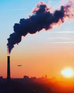 A factory with plumes of smoke against a sunset