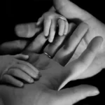 a black and white shot of an adult hands and baby hands family