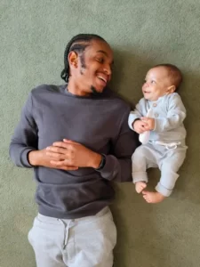 A man and his baby lygin on the floor smiling at each other