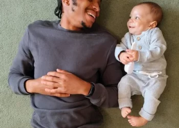 A man and his baby lygin on the floor smiling at each other