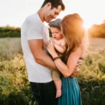 A man and woman holding a baby at sunset