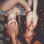two women lyind down with their hands over each others eyes